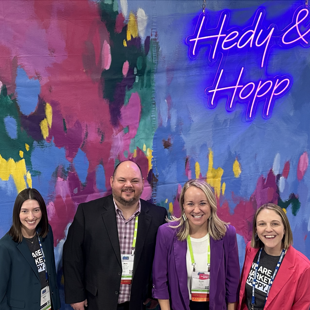 Four Hedy & Hopp employees standing in front of a hand-painted backdrop by Jessica Hitchcock.